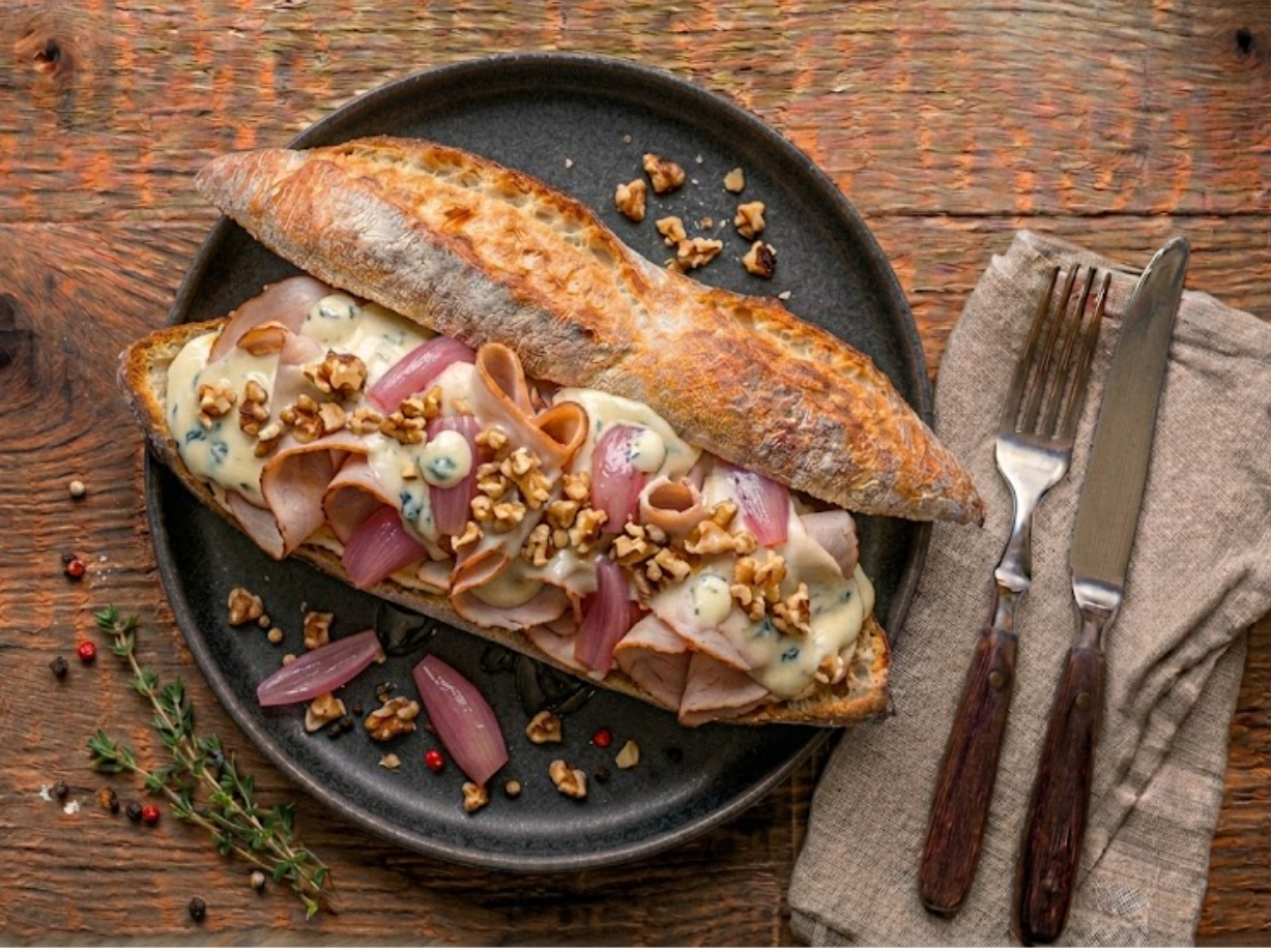 Sandwich L'Auvergnat — fines tranches de dinde fumée roulées, mascarpone au bleu, pickles d'échalote rouge au vinaigre de miel, noix concassées, thym frais sur baguette tradition.