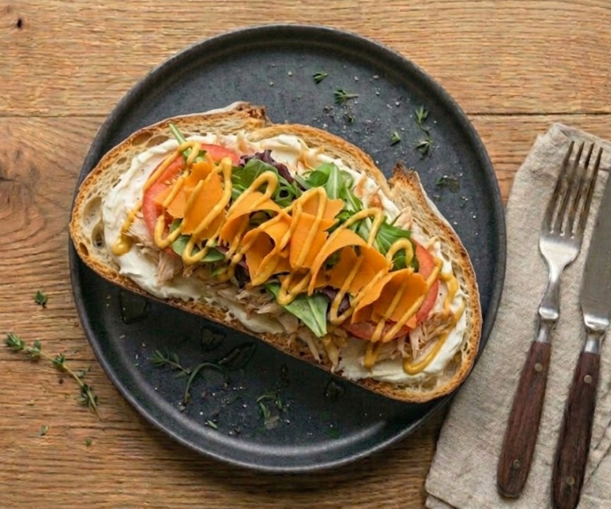 Tartine La Kepew — pain de campagne, cream cheese, poulet rôti effiloché, jeunes pousses, rondelles de tomate, copeaux de mimolette, filets de moutarde au miel.